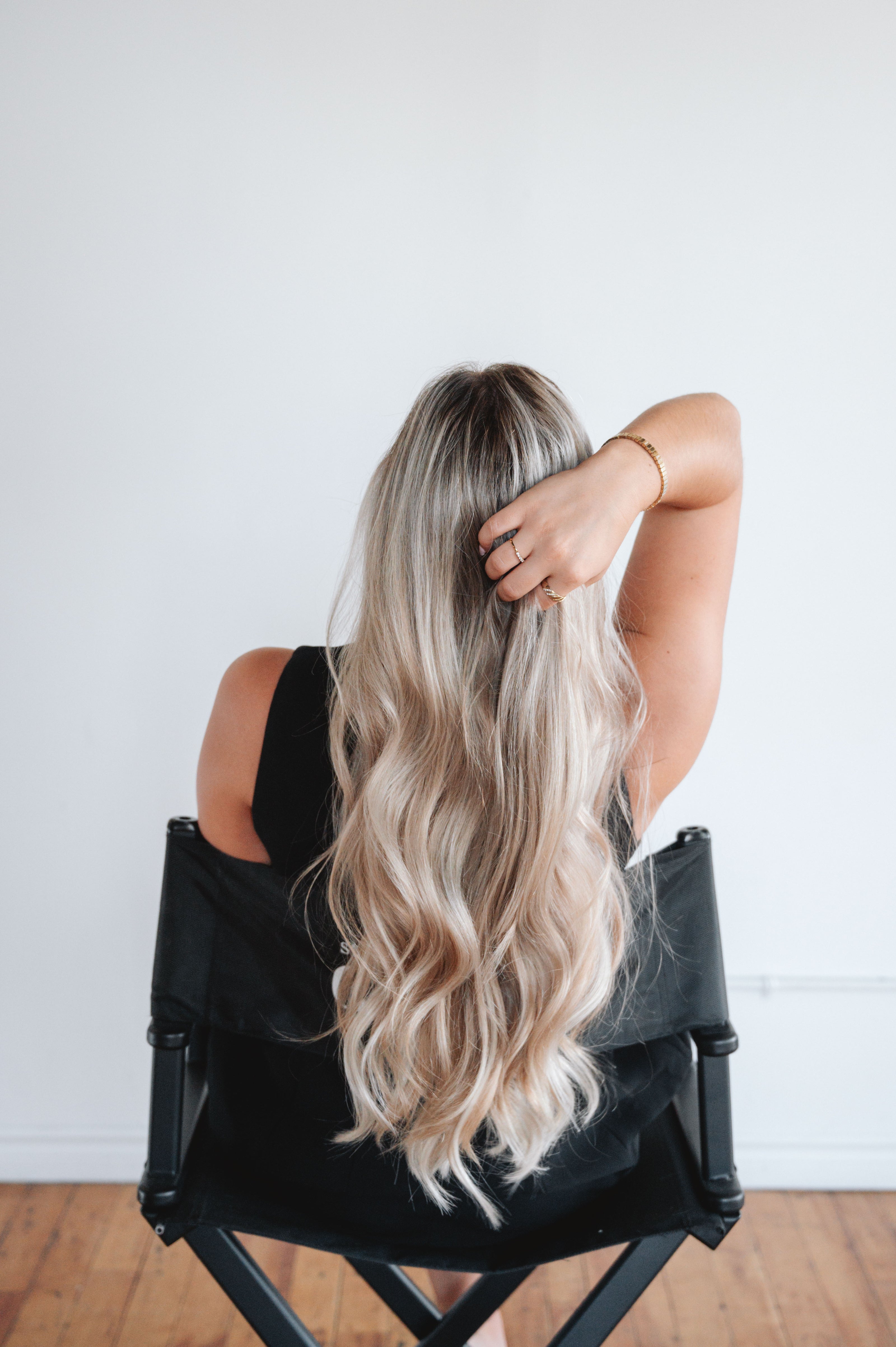model wear 24'' of hair extensions in blonde sitting in a director chair holding her hair from the back, in a studio in Montreal. Seamless hair extensions and gorgeous look. 