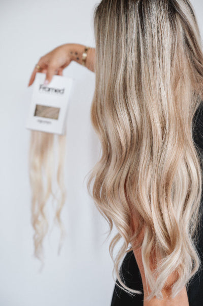 Model blond long hair holding box with clip in hair extensions in a white studio wearing invisible hair extensions clip in 